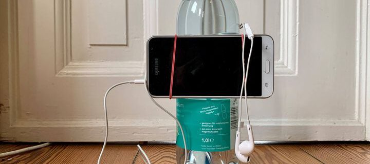 Das Bild zeigt, wie ein Smartphone mit einem Gummiring an der Wasserflasche befestigt ist. Solch ein einfaches Stativ ist für viele Situationen völlig ausreichend.